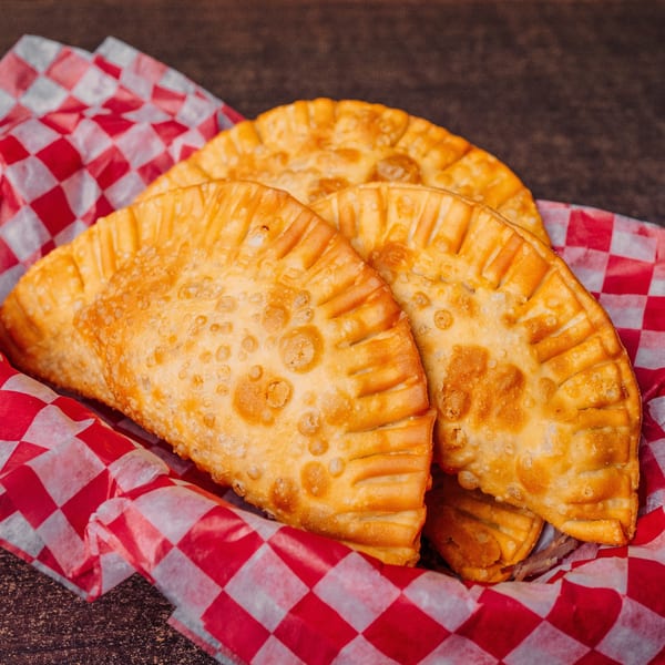 Three golden-brown El Cerro empanadas with crimped edges, nestled in red and white checkered paper.