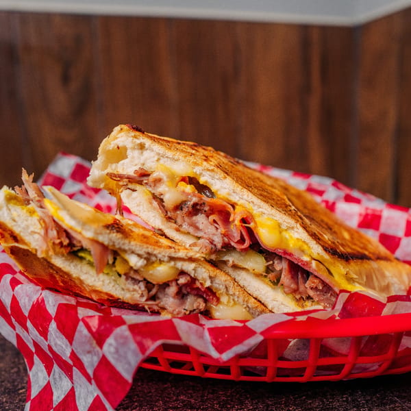 A Cuban sandwich, cut in half, with melted cheese and meat, served in a red basket.